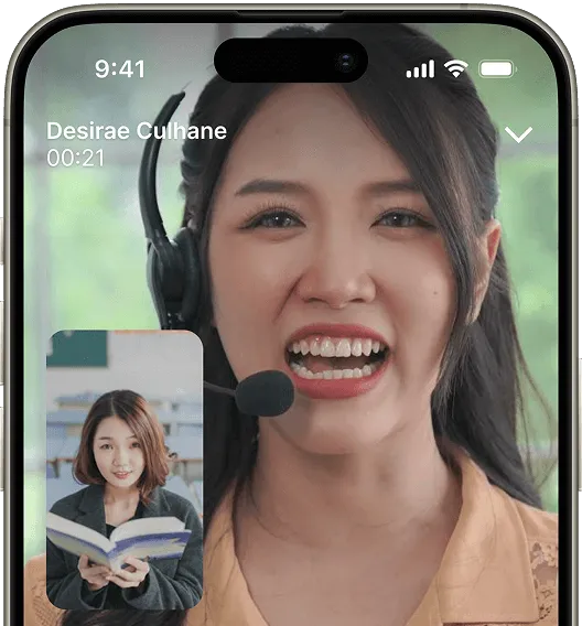 A smartphone screen displays a video call interface showing a person wearing headphones, with a smaller image of another person reading.