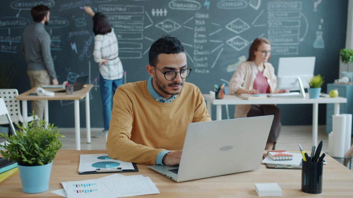Man working on laptop in modern office with colleagues