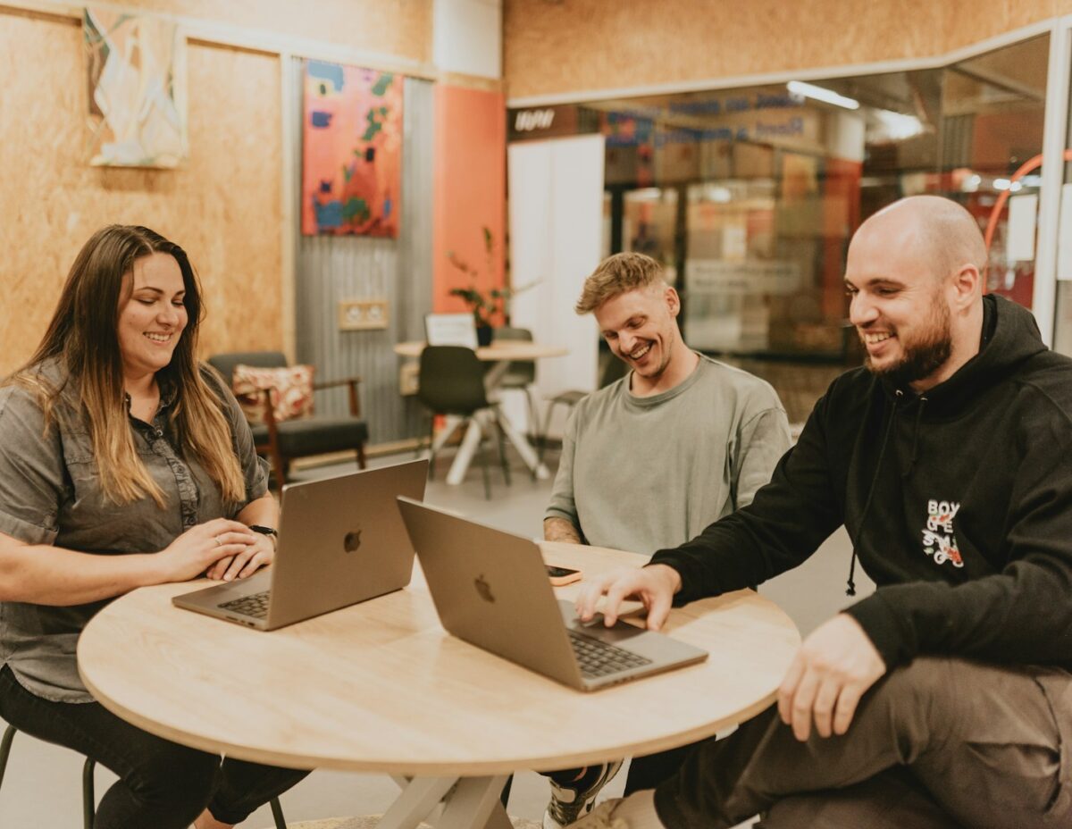 Three people collaborate around a table with laptops