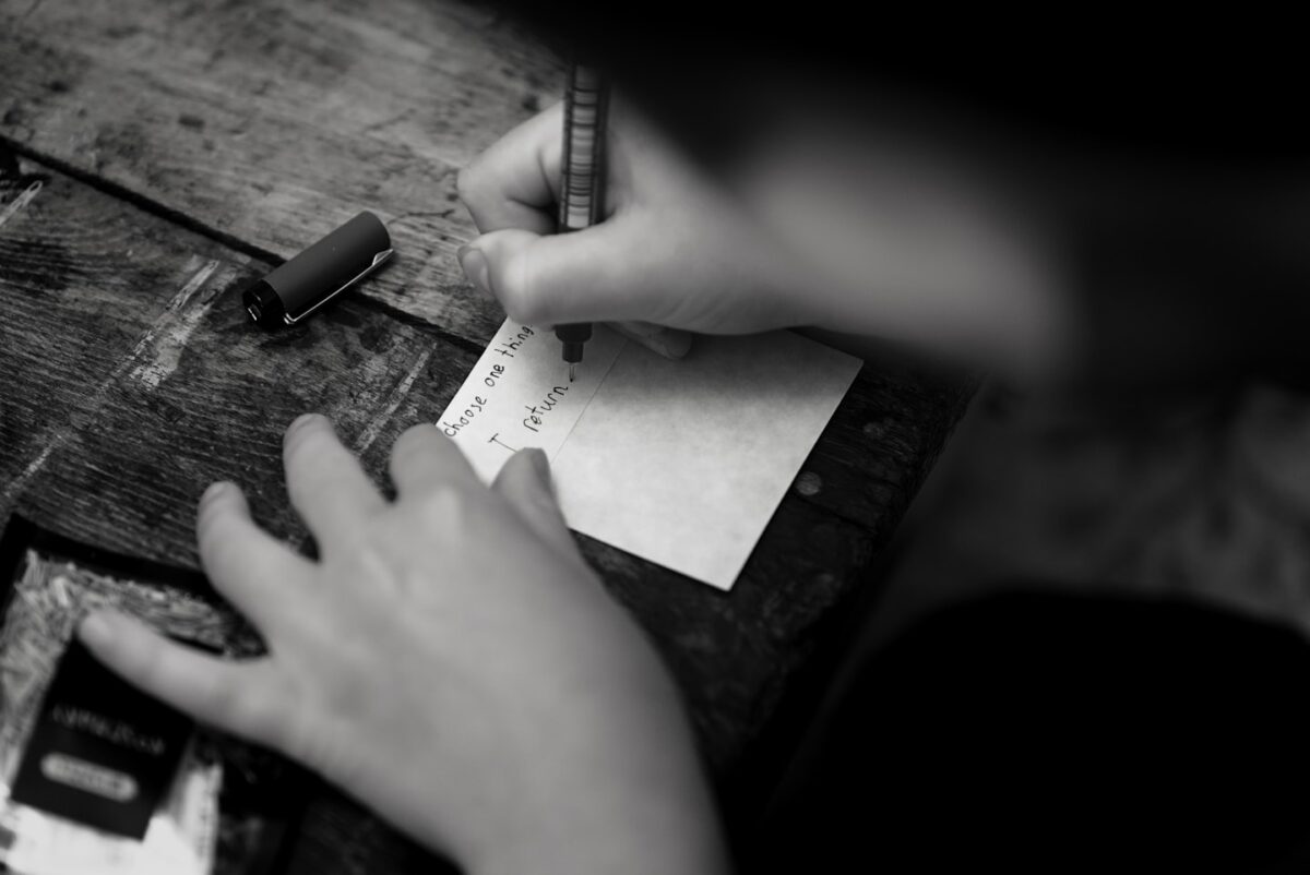 A person writing on a small card with a pen on a wooden table