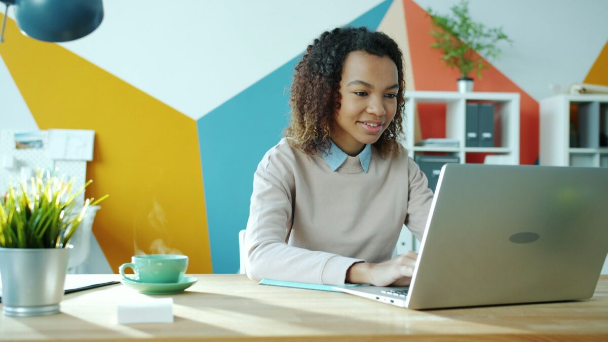 A smiling woman works on a laptop at a desk
